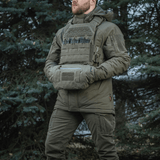 Mies pukeutuneena taktiseen varustukseen ja M-Tac Taktisk Håndvarmer Elite metsäympäristössä