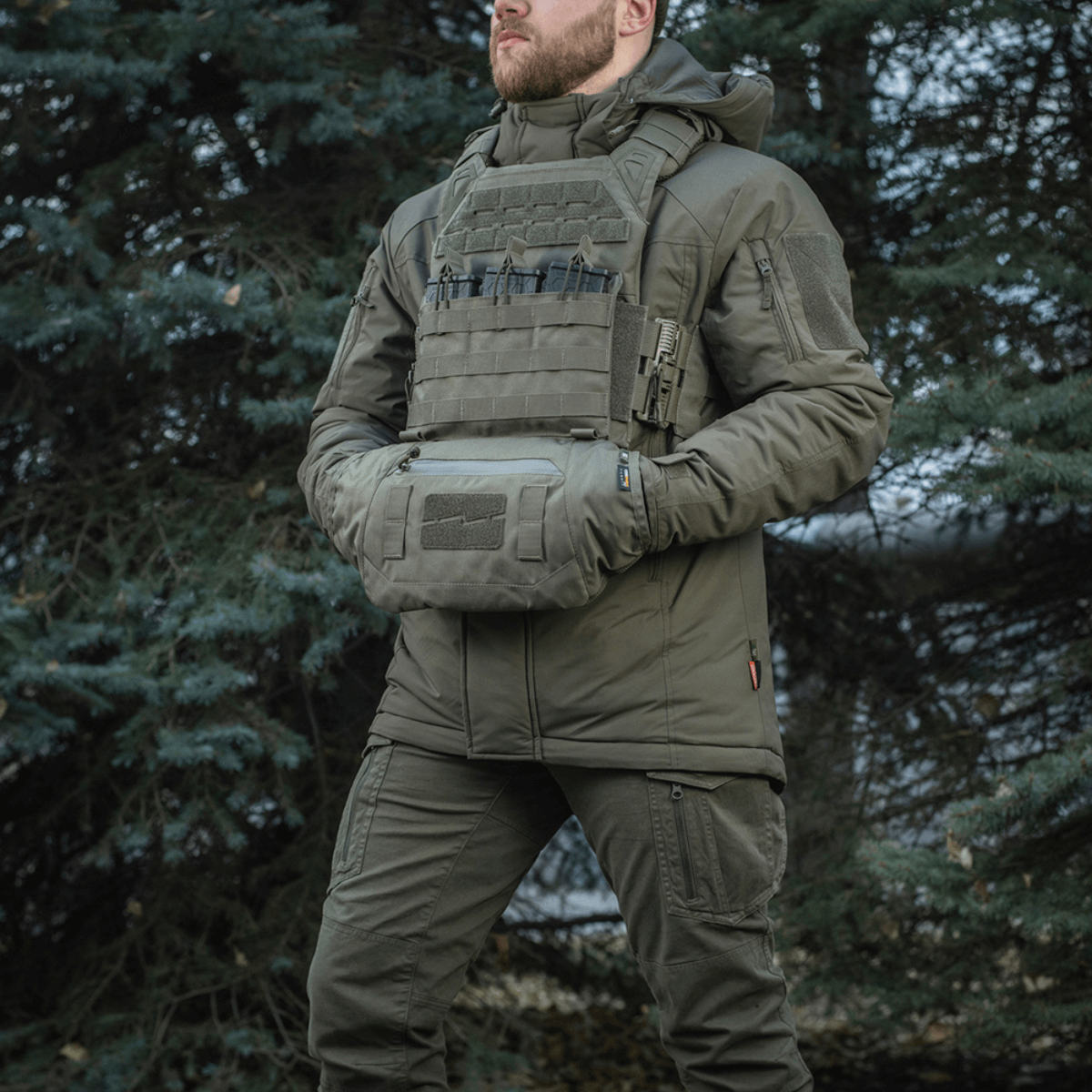 Mies pukeutuneena taktiseen varustukseen ja M-Tac Taktisk Håndvarmer Elite metsäympäristössä