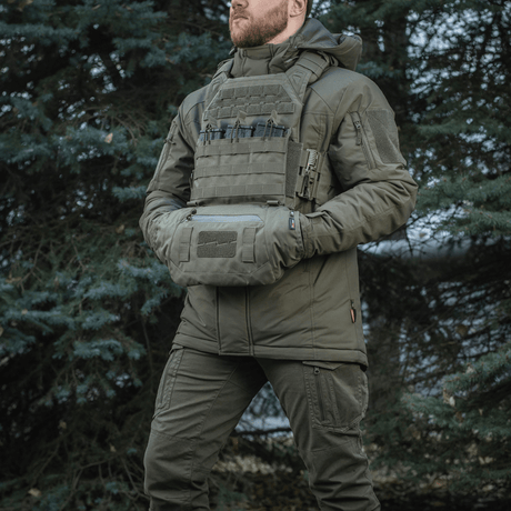 Mies pukeutuneena taktiseen varustukseen ja M-Tac Taktisk Håndvarmer Elite metsäympäristössä