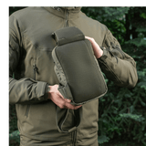 Henkilö esittelee M-Tac Sling Pistoltaske Elite Hexiä ulkona metsäympäristössä, takki vetoketjulla.