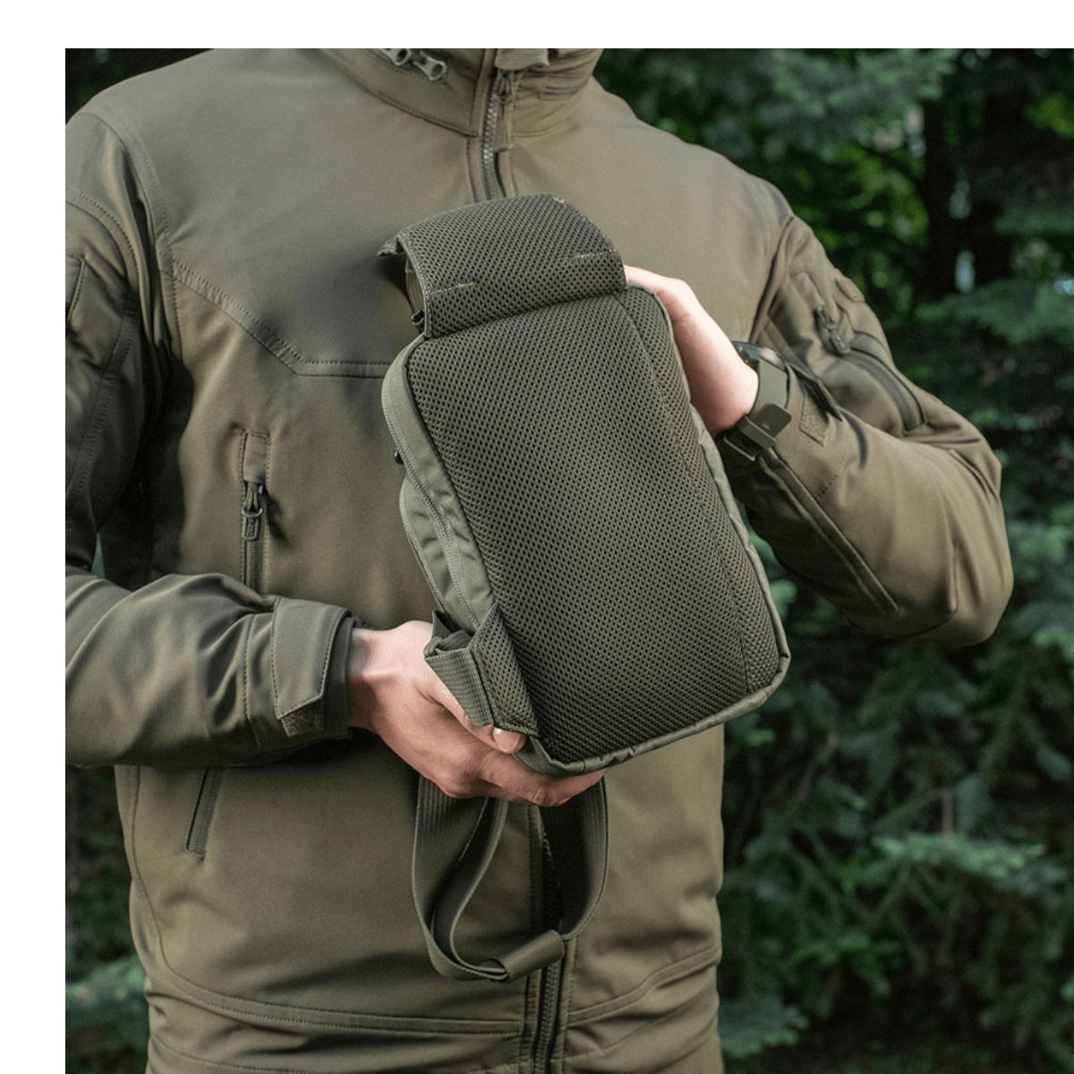 Henkilö esittelee M-Tac Sling Pistoltaske Elite Hexiä ulkona metsäympäristössä, takki vetoketjulla.