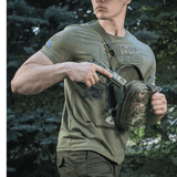 Mies kantaa M-Tac Sling Pistoltaske Elite Hexiä piilotetun aseen kanssa metsässä.