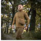 Mies metsässä M-Tac Admin-laukku Eliten kanssa, pukeutunut taktisiin vaatteisiin, säädettävä olkahihna, kestävä Cordura, luonnontausta