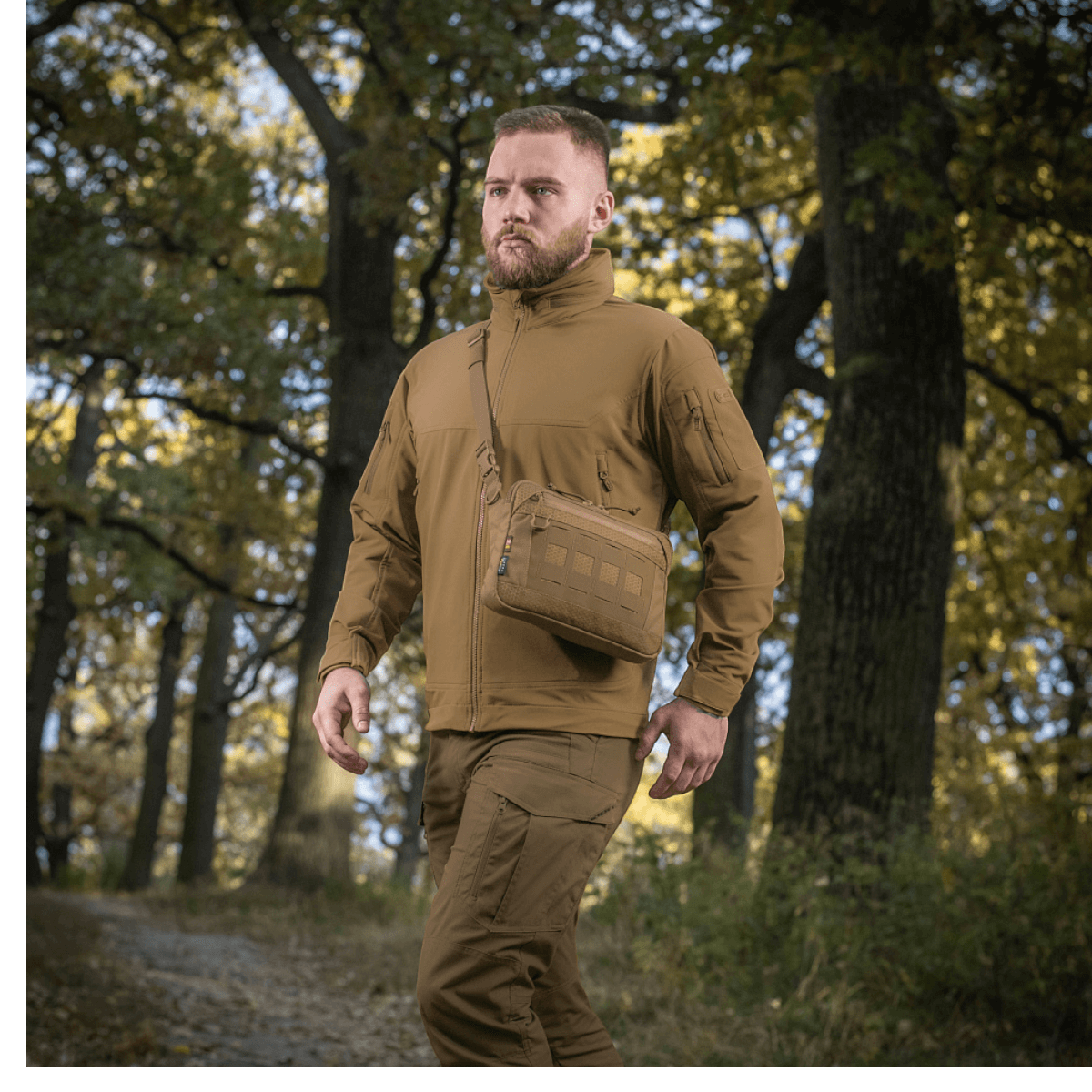 Mies metsässä M-Tac Admin-laukku Eliten kanssa, pukeutunut taktisiin vaatteisiin, säädettävä olkahihna, kestävä Cordura, luonnontausta