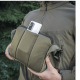 M-Tac Admin Taske Elite Cordura-kankaasta, älypuhelin taskussa, säädettävä olkahihna ja tukeva rakenne, ulkoilmataustalla.