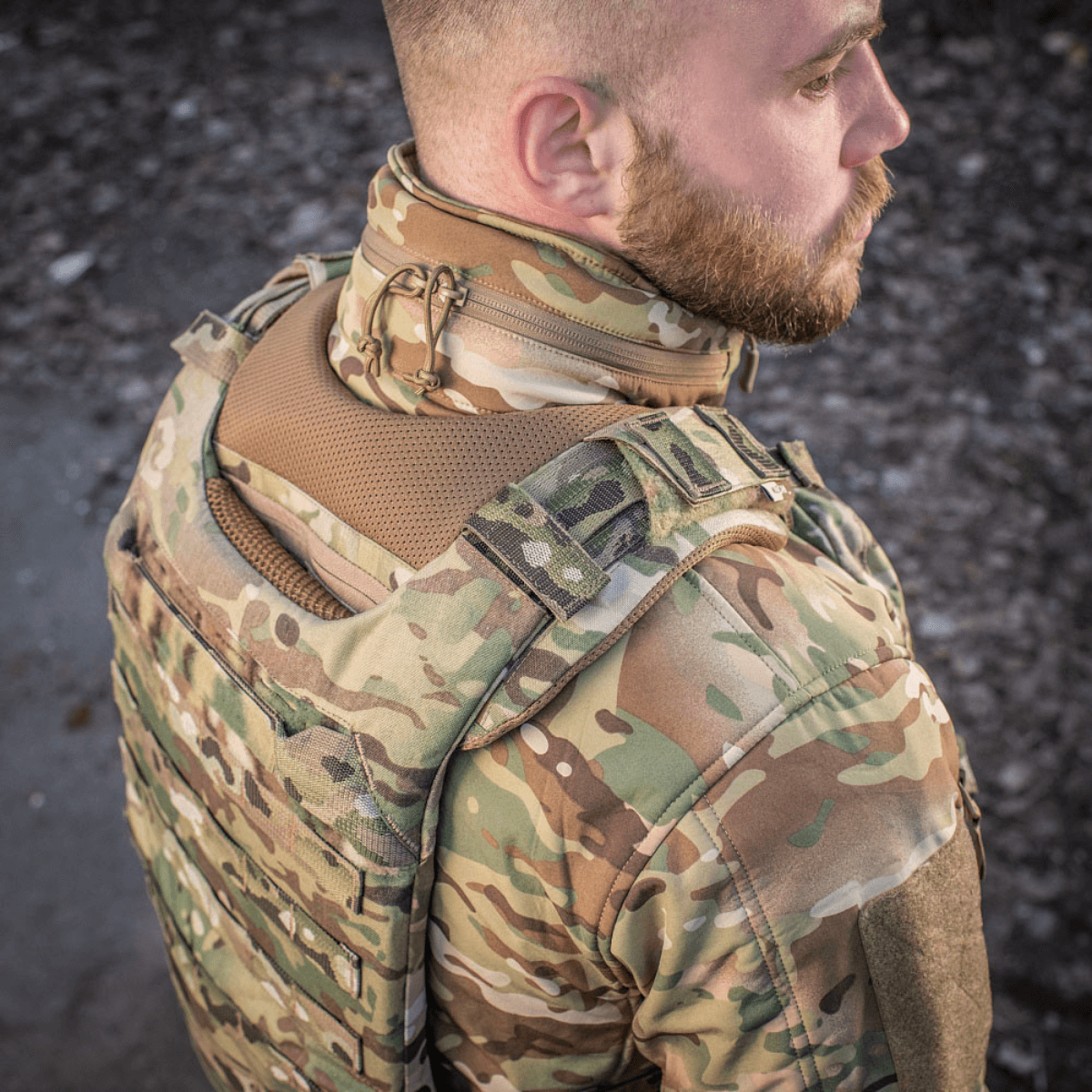 Henkilö pukeutuneena M-Tac olkapääpehmusteeseen Plate Carrier Cuirass QRS:lle camokuosissa, Cordura-materiaali mukavuuteen ja kestävyyteen.