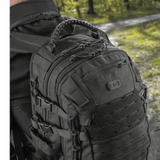 Mies käyttää M-Tac Mission Pack Elite -reppua ergonomisella muotoilulla ja MOLLE LASER CUT-systemillä metsäympäristössä.
