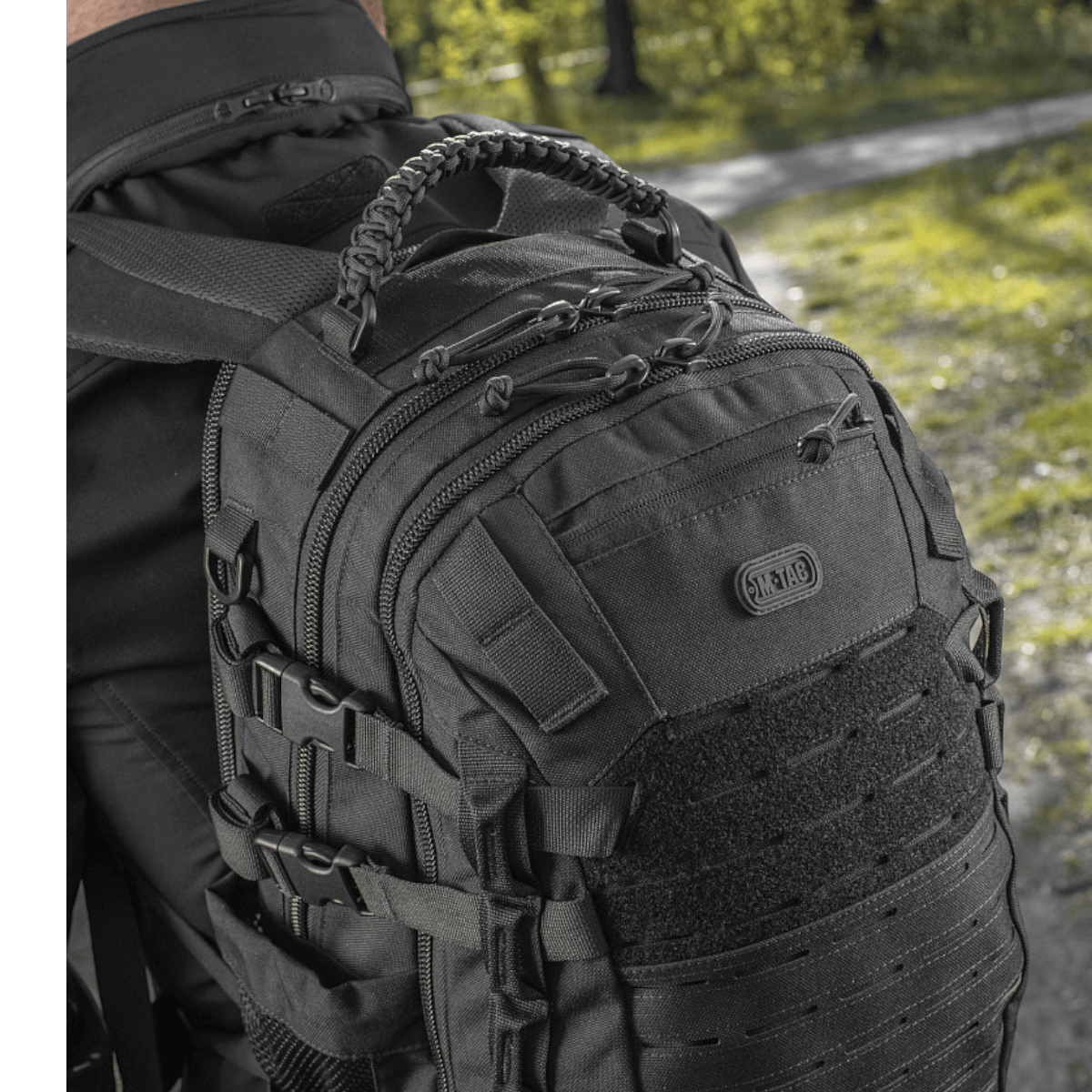 Mies käyttää M-Tac Mission Pack Elite -reppua ergonomisella muotoilulla ja MOLLE LASER CUT-systemillä metsäympäristössä.