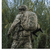 Sotilas kantaa M-Tac Mission Pack Elite -reppua camo-kuvioituna luonnossa.