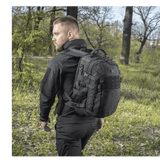 Mies kantaa M-Tac Mission Pack Elite -reppua luonnossa, korostaen ergonomista muotoilua ja Cordura 1000D -materiaalia.
