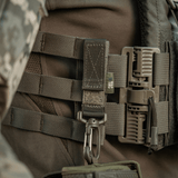 M-Tac karabiinihaka-lisävaruste kiinnitetty taktiseen MOLLE-reppuun lisävarusteille. Säädettävä Velcro-remmi kiinnitystä varten.