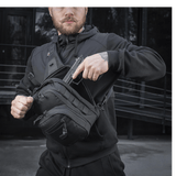 Mies käyttää M-Tac Cross Taske Slim Elite Hex -laukkua mustana Cordura-materiaaleilla, vetoketjuilla ja YKK- ja Woojin-soljilla, ulkoilmassa.