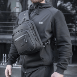 Henkilö kantaa M-Tac Cross Taske Slim Elite Hex -laukkua, pukeutunut mustiin, ulkona.