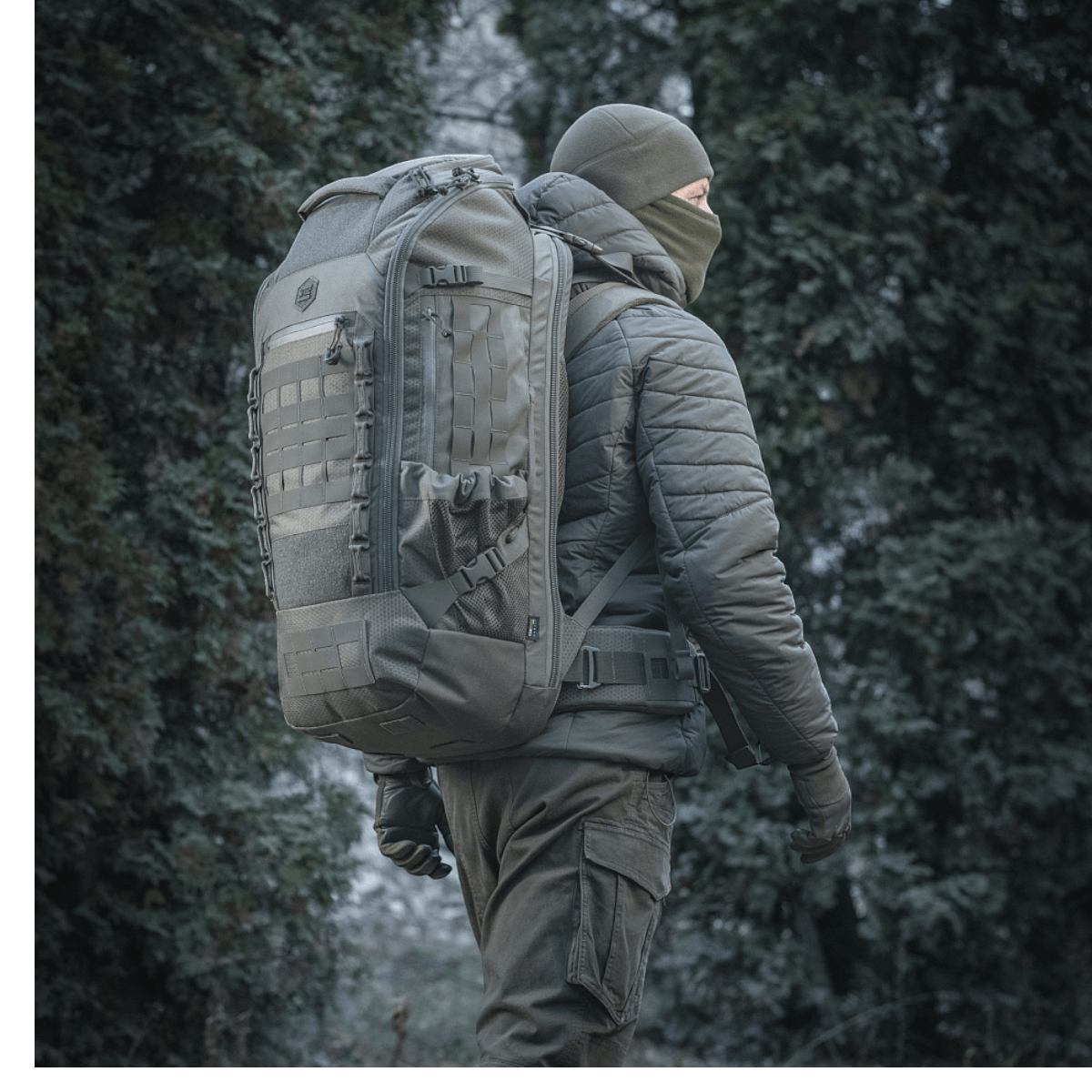 M-Tac reppu Large Elite Hex Gen. IV metsäympäristössä, suunniteltu aseiden kantamiseen ja suojaamiseen kestävästä Cordura-materiaalista.