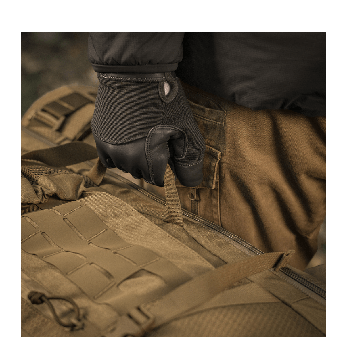 Käyttäjä hanskat kädessä pitää M-Tac reppu Large Elite Hex Gen. IV, tehty Cordura 500D- ja Hex 1000 -materiaaleista.