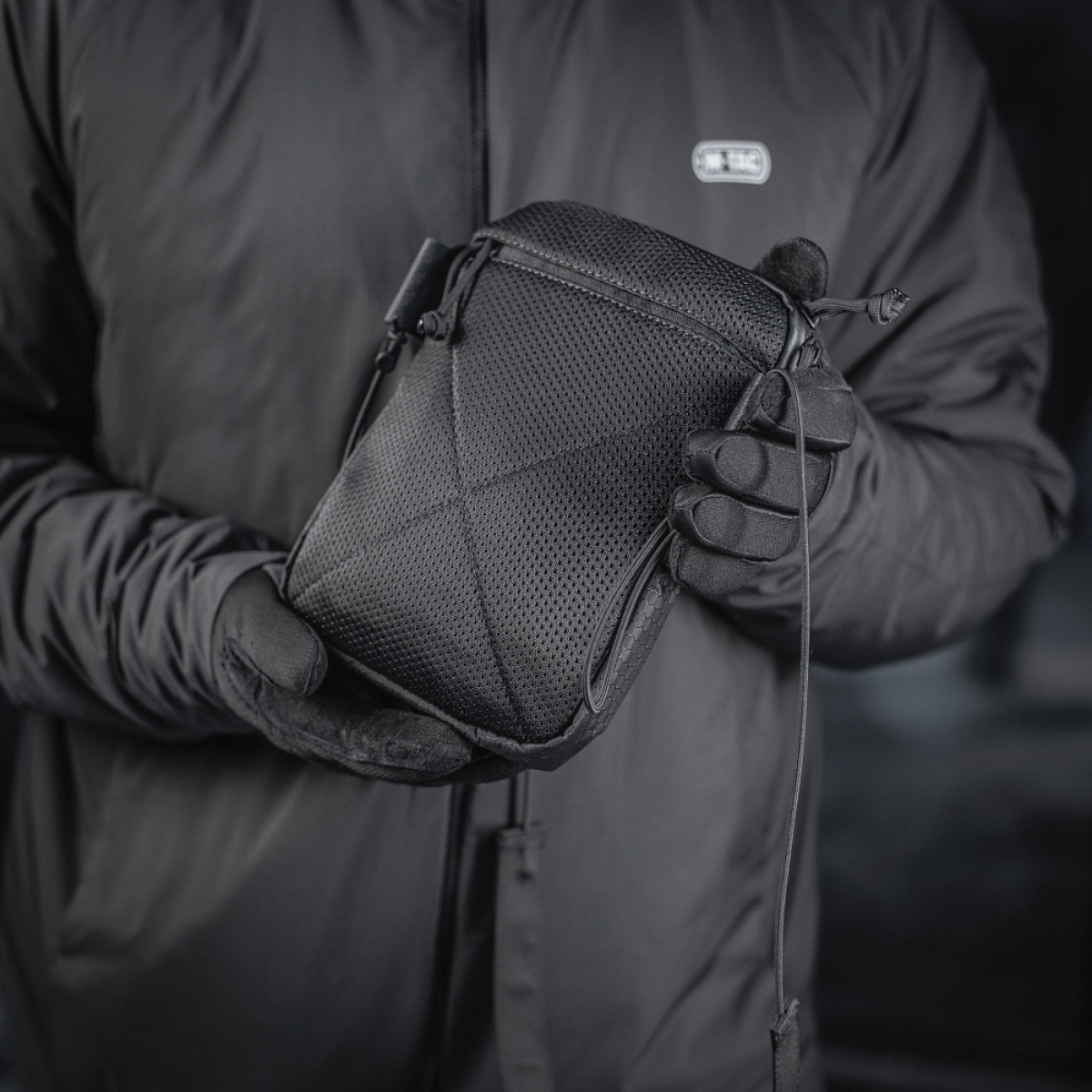 M‑Tac Pocket Bag Elite HEX musta, pidetään henkilön toimesta, jolla on käsineet. Kompakti laukku erilaisten pikkutarvikkeiden säilytykseen.
