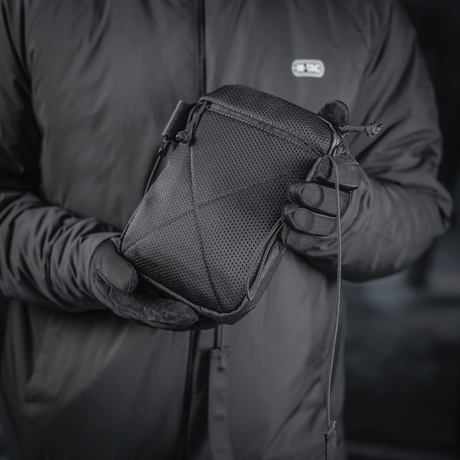 M‑Tac Pocket Bag Elite HEX musta, pidetään henkilön toimesta, jolla on käsineet. Kompakti laukku erilaisten pikkutarvikkeiden säilytykseen.