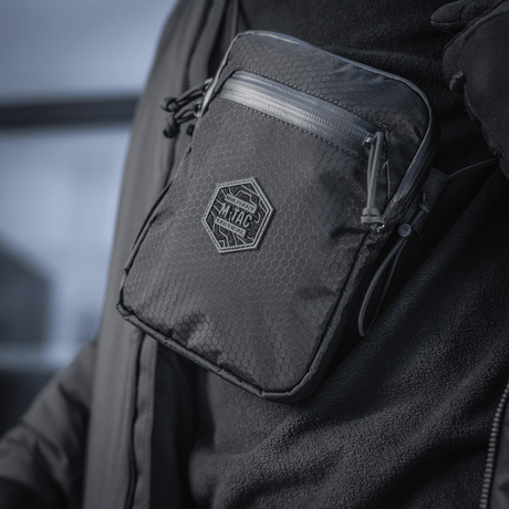 Henkilö kantaa pientä, vankkaa M‑Tac Pocket Bag Elite HEX:ää kulutusta kestävin YKK-vetoketjuin, sopii arjen säilytystarpeisiin.