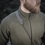Mies kantaa vihreää fleecetakkia, M‑Tac Pocket Bag Elite HEX -hihna olkapäällä, näyttää kestävyyttä ja tyyliä.