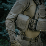 M-Tac Medic Pouch Vertical Large Elite kiinnitettynä taktiseen liiviin metsässä, tarjoaa kestävän säilytyksen ensiapuvälineille.