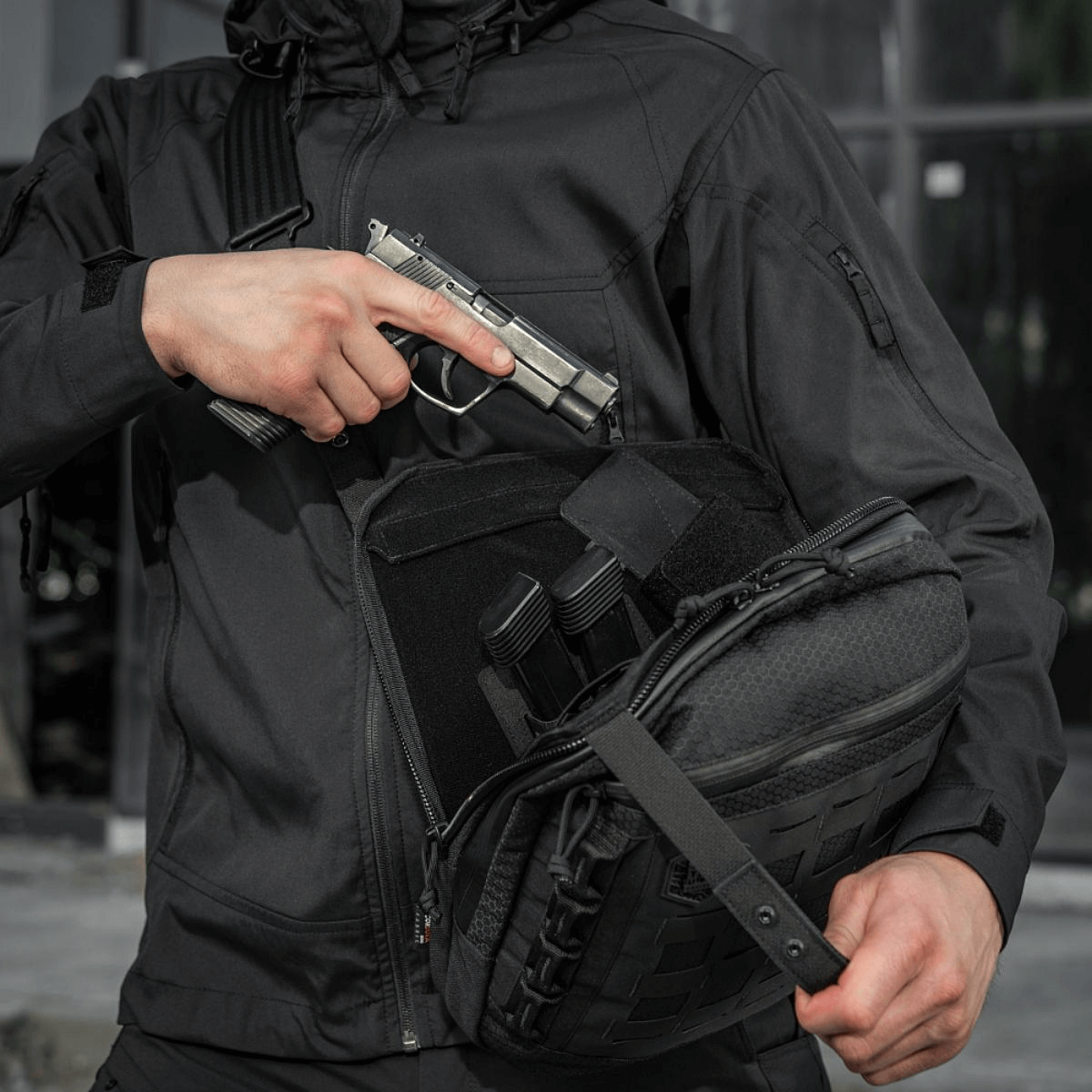 M-Tac Tablet Bag Laser Cut Hex piilotetulla pistoolitaskulla ja modulaarisilla insertillä, käytössä taktillisessa tilanteessa henkilöllä mustassa vaatetuksessa.