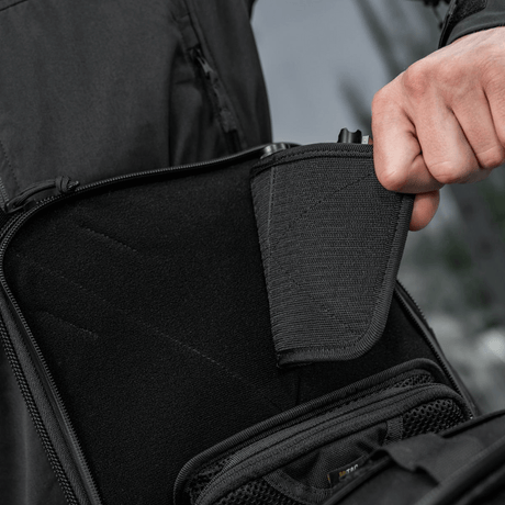 Henkilö osoittaa piilotetun aseen lokeroa M-Tac Tablet Bag Laser Cut Hexissä modulaarisilla inserteillä ja nopean pääsyn suunnittelulla.