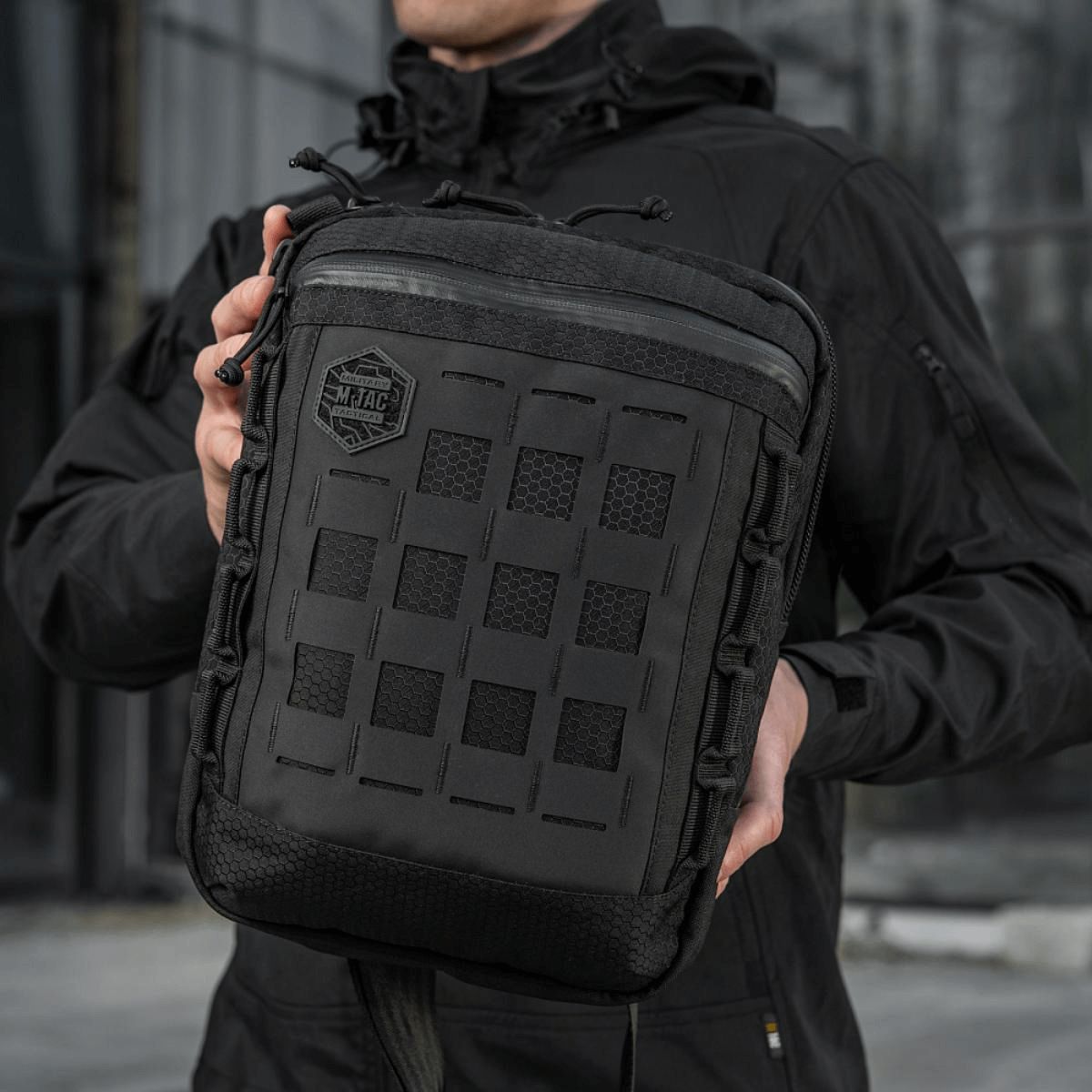 Mies pitää M-Tac Tablet Bag Laser Cut Hex -laukkua, valmistettu Cordurasta, Laser Cut MOLLE -paneeli edessä.