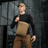 Mies kantaa M-Tac Tablet Bag Laser Cut Hex edessä toimistorakennusta, huomaamaton olkalaukku EDC:lle ja asiakirjoille.