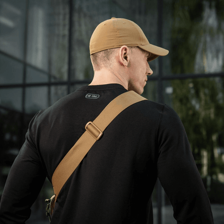Mies mustassa paidassa ja beigessä lippiksessä nähtynä takaa, M-Tac Tablet Bag Laser Cut Hex vinosti olkapäällä.