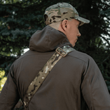 Mies kantaa M-Tac Tablet Bag Laser Cut Hex -laukkua camo-olkahihnalla luonnonympäristössä.