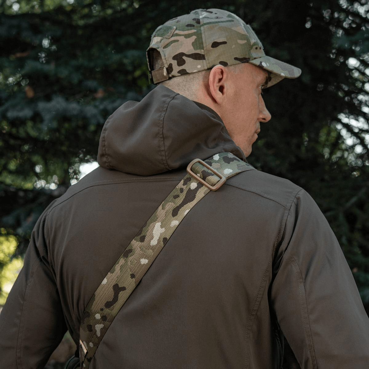 Mies kantaa M-Tac Tablet Bag Laser Cut Hex -laukkua camo-olkahihnalla luonnonympäristössä.