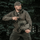 Henkilö M-Tac Tablet Bag Laser Cut Hex -laukulla, näyttää nopean pääsyn ja piilotetun asekotelon, metsätausta.