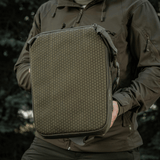 M-Tac Tablet Bag Laser Cut Hex pidetään henkilön toimesta, Cordura-materiaalia, MOLLE-etupaneeli, sopii EDC:hen, tableteille ja asiakirjoille.