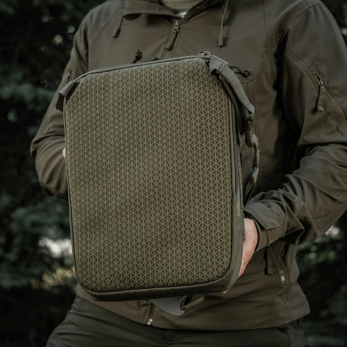 M-Tac Tablet Bag Laser Cut Hex pidetään henkilön toimesta, Cordura-materiaalia, MOLLE-etupaneeli, sopii EDC:hen, tableteille ja asiakirjoille.