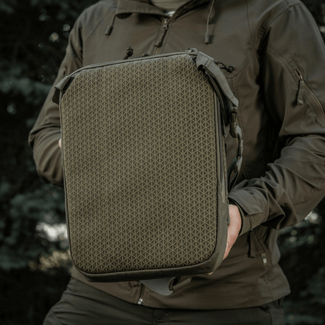 M-Tac Tablet Bag Laser Cut Hex pidetään henkilön toimesta, Cordura-materiaalia, MOLLE-etupaneeli, sopii EDC:hen, tableteille ja asiakirjoille.