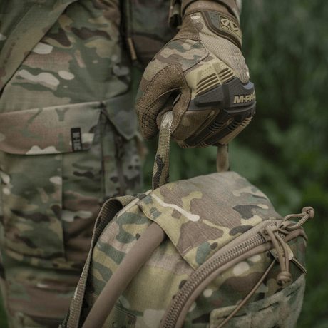 M-Tac STURM Elite -reppu camo-muotoilulla ja MOLLE-järjestelmällä, pidetty henkilön toimesta armeijavaatteissa ja taktisisissa käsineissä, 15 l tilavuus.