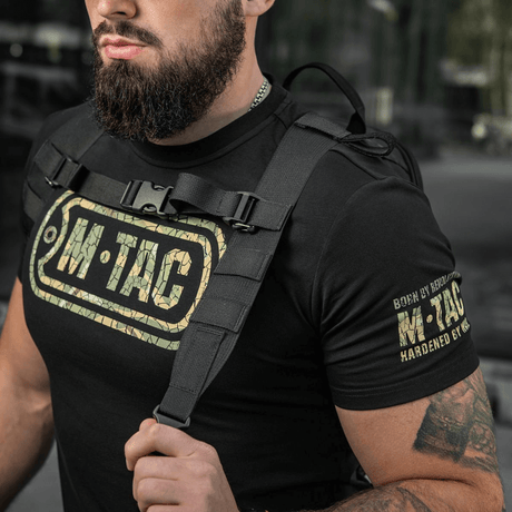Mies kantaa M-Tac STURM Elite -reppua taktisine hihnoineen ja M-Tac-logolla t-paidassa, sopii lyhyille retkille.