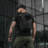 Mies kantaa M-Tac STURM Elite -reppua 15 l, musta väri, suunniteltu lyhytaikaisiin kenttäoloihin, MOLLE Laser Cut -paneelilla.