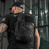 Mies kantaa M-Tac STURM Elite -reppua MOLLE Laser Cut -etupaneelilla urbaanissa ympäristössä, taktinen ja kestävä, suunniteltu lyhytaikaisiin kenttäretkiin.