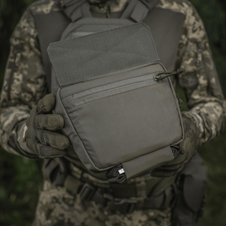 M-Tac Large Elite Gen.II olkalaukku maastokuvioidussa asussa olevan henkilön kädessä, valmistettu Cordura 500D:stä, YKK-vetoketjut.