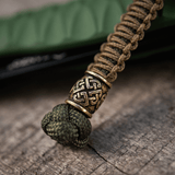 M-Tac Knife Lanyard Celtic, punottu paracord kelttikuvioinnilla, veitsilisävaruste puumaisella pinnalla.