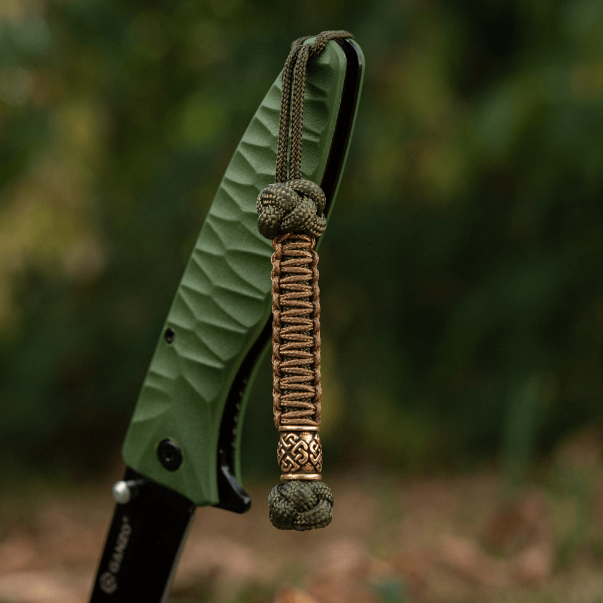 M-Tac Knife Lanyard Celtic, punottu paracord-veitsilisävaruste, korostaa tyyliä ja käytännöllisyyttä ulko- ja arkioloissa.
