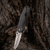 M-Tac Knife Lanyard Celtic, punottu paracord, asennettuna veitseen rustiikilla taustalla.