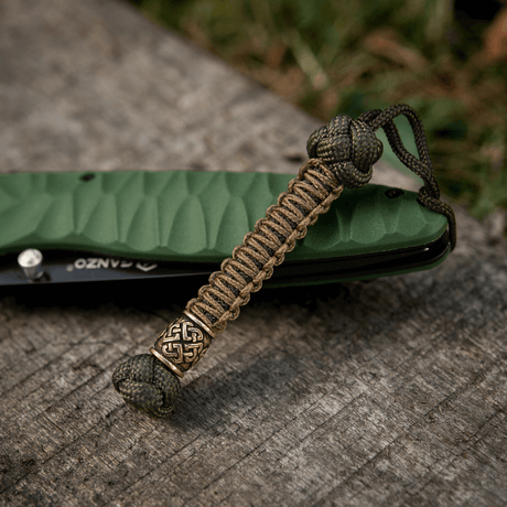 M-Tac Knife Lanyard Celtic, punottu paracord vihreän taskuveitsen vieressä puupinnalla.