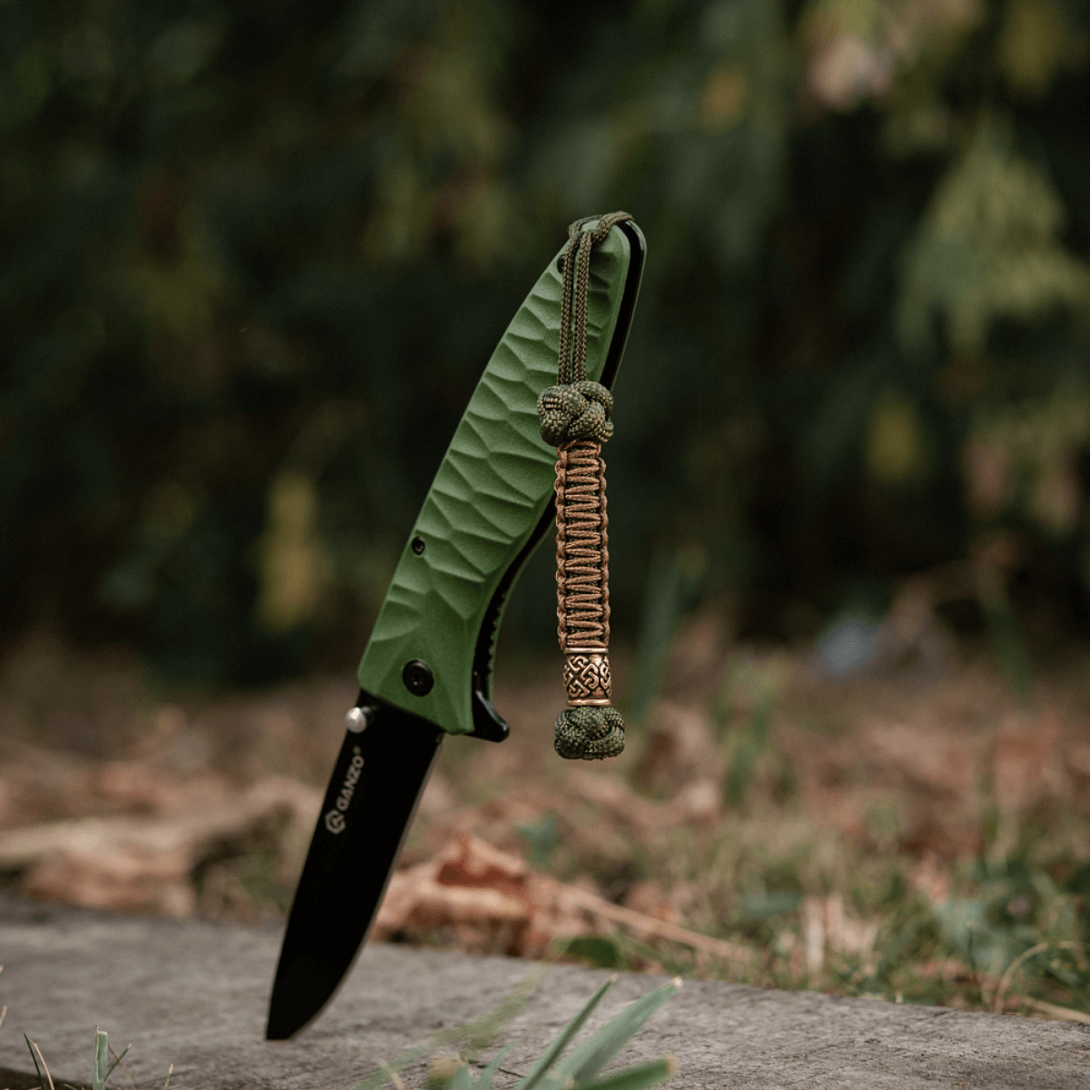M-Tac Knife Lanyard Celtic - vihreä taittoveitsi punotulla paracord-lanyardilla ulkoilmassa.