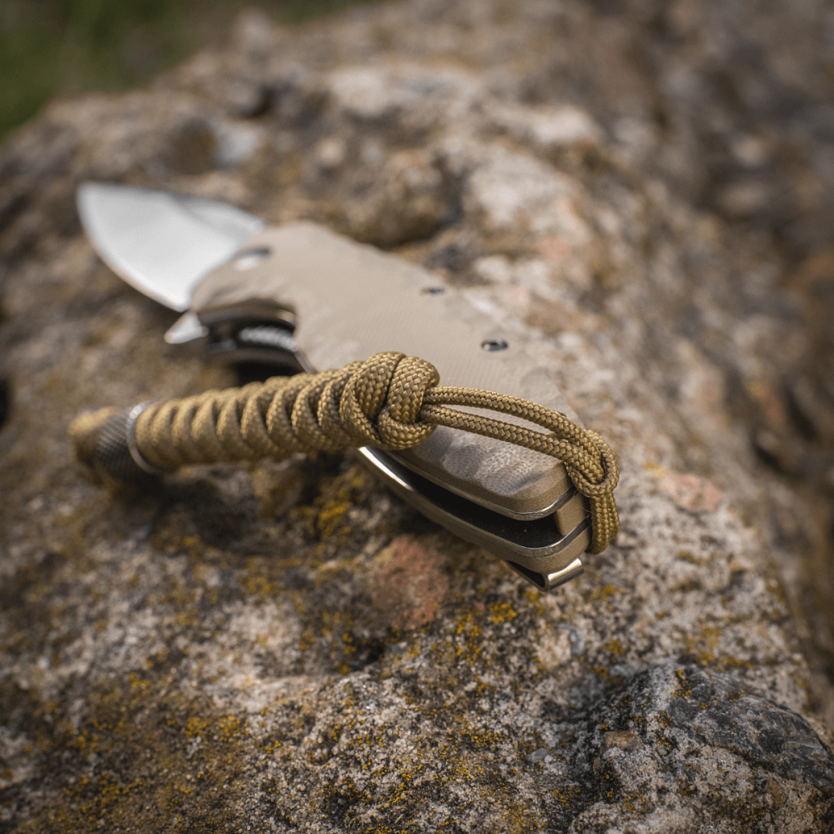 M-Tac Viper Lanyard Stainless Steel kiinnitettynä veitselle, esillä kivilaatalla. Joustava jatko-osa punotusta paracordista.