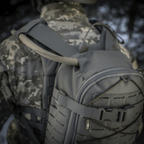 M-Tac Sturm Elite Gen.II harmaasta Cordurasta sotilaan päällä, näyttää sisäänrakennetun juomajärjestelmän letkun luonnossa.