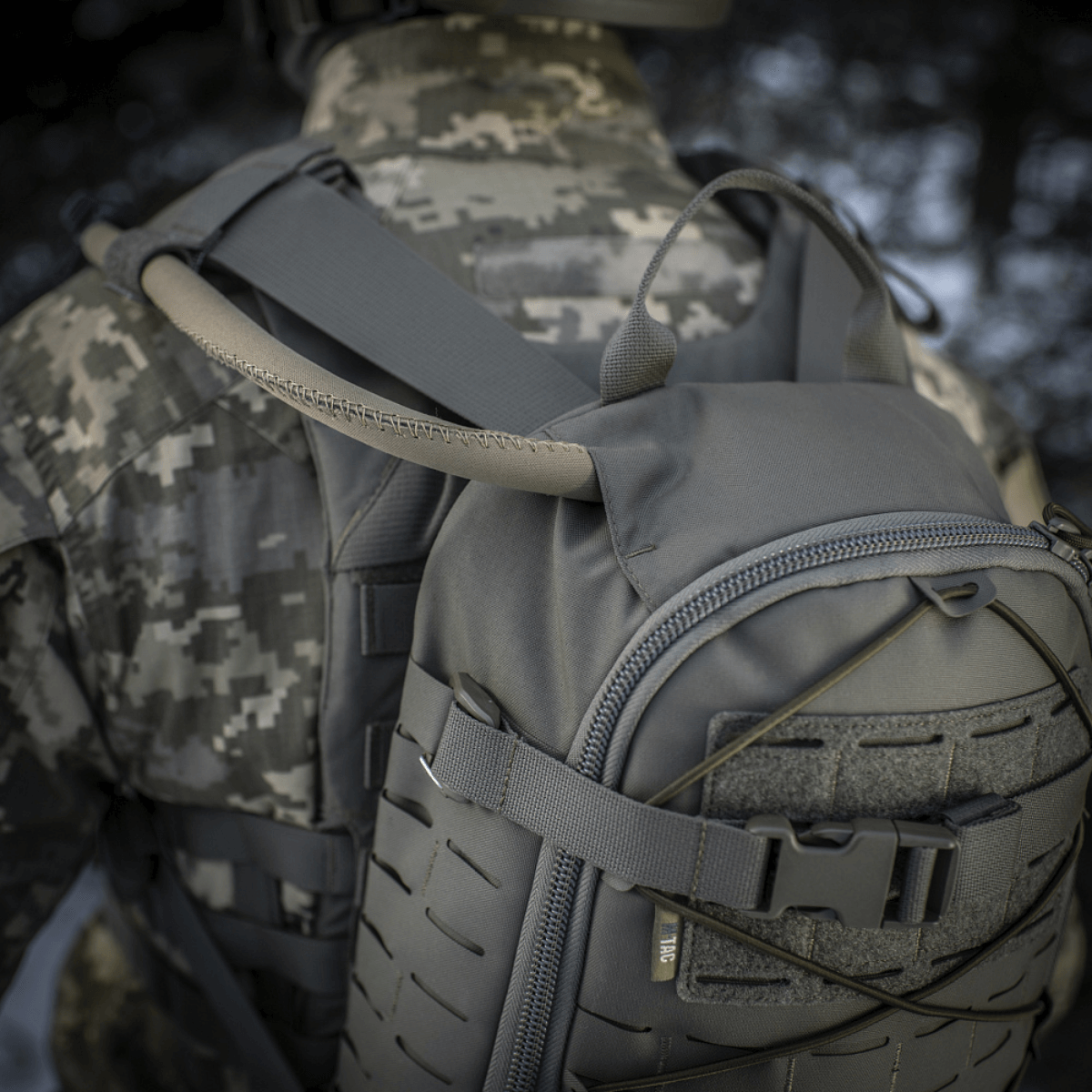 M-Tac Sturm Elite Gen.II harmaasta Cordurasta sotilaan päällä, näyttää sisäänrakennetun juomajärjestelmän letkun luonnossa.