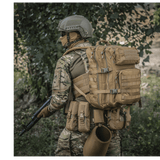 M-Tac Large Assault Pack -reppu MOLLE-järjestelmällä, kantaja maastokuosisessa univormussa puiden alla.