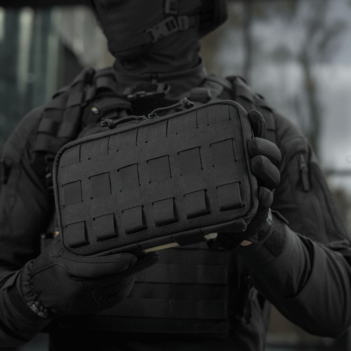 Henkilö pitelee M-Tac Admin Pouch Large Eliteä mustana, toimiva laukku taktisiin varusteisiin, Cordura 500D, tarrat ja laser-leikkaukset.